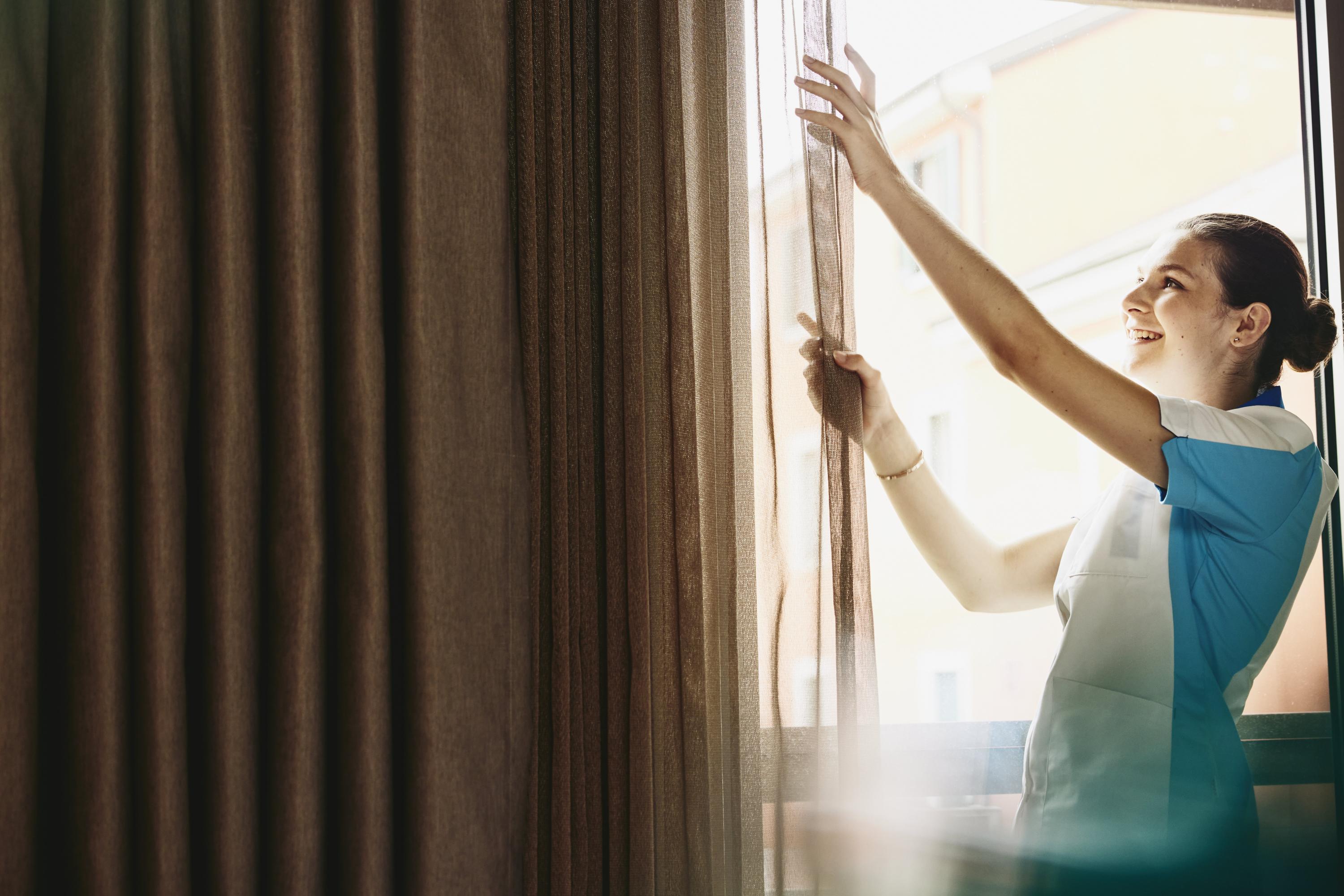 Smiling woman closing/opening curtains in a hotel room.