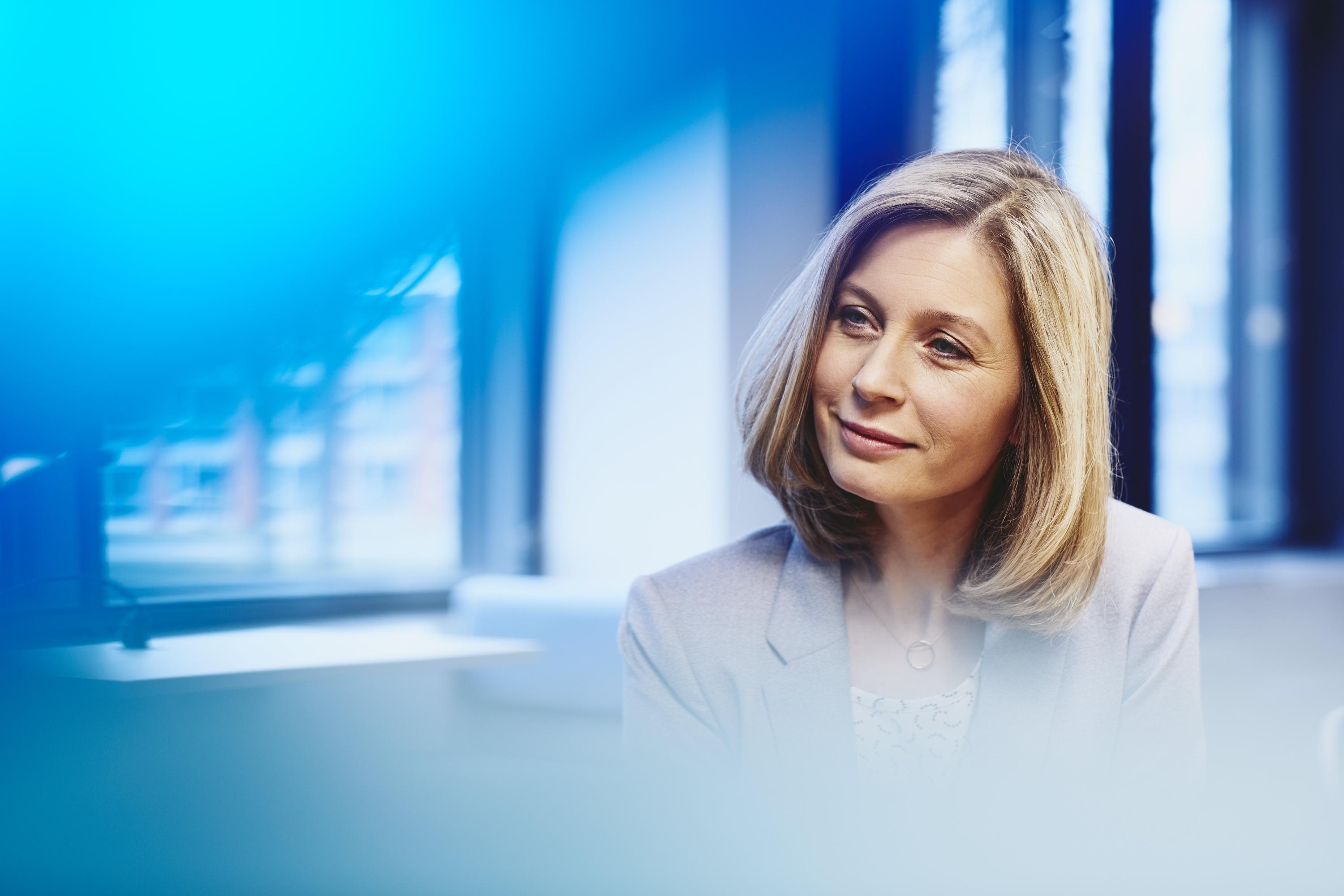 Business woman in an office smiling. Primary color: blue