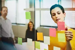Two business female and a male in an office putting sticky notes on a window.

