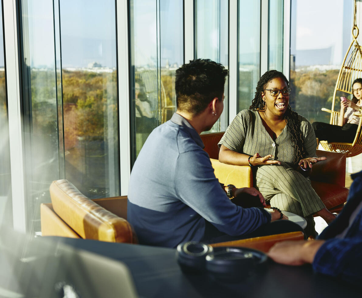 Two people having a conversation while sitting down in a lounge environment.
Two people having a conversation while sitting down in a lounge environment.