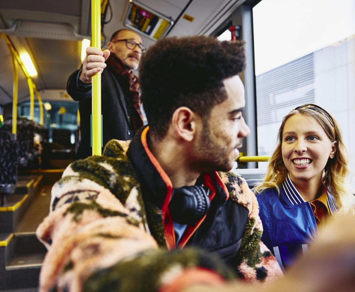 Woman and boy having a conversation, smiling, sitting in a bus. Other people in the background.