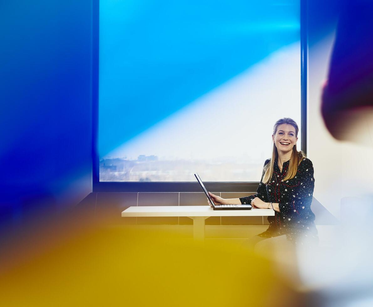 Woman smiling with laptop near window with city view.