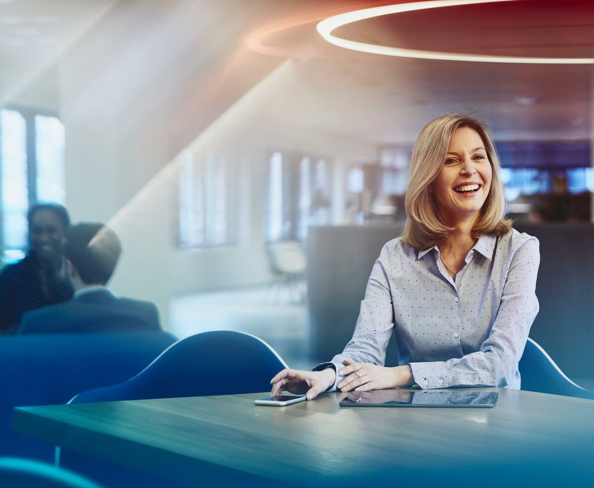 Business woman at a desk with her phone and tablet, smiling. Primary color: blue. Business woman at a desk with her phone and tablet, smiling. Primary color: blue.