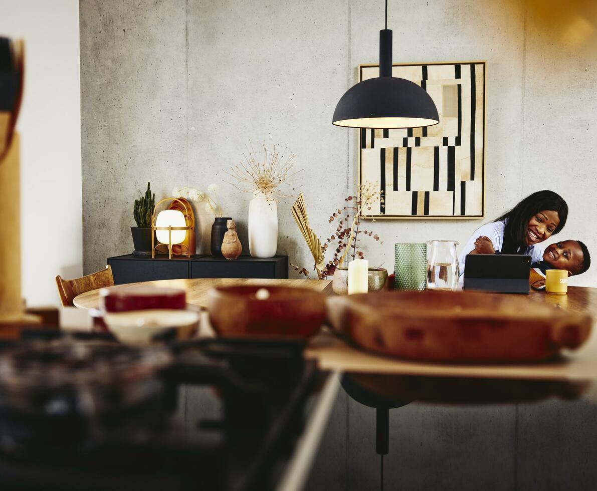 Smiling woman with kid on her lap sitting at a the kitchen table with tablet.