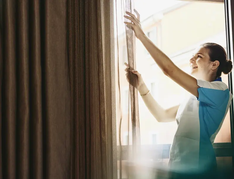 Smiling woman closing/opening curtains in a hotel room.