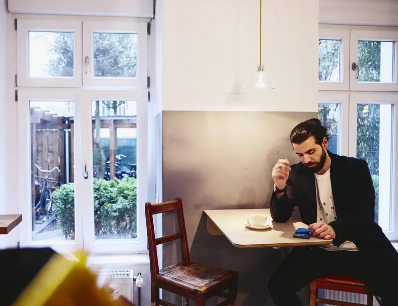 Man sitting at table with a coffee, looking seriously at his phone.