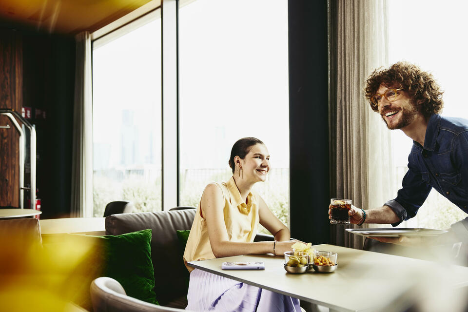 Waiter serving a drink to female sitting at a table.
