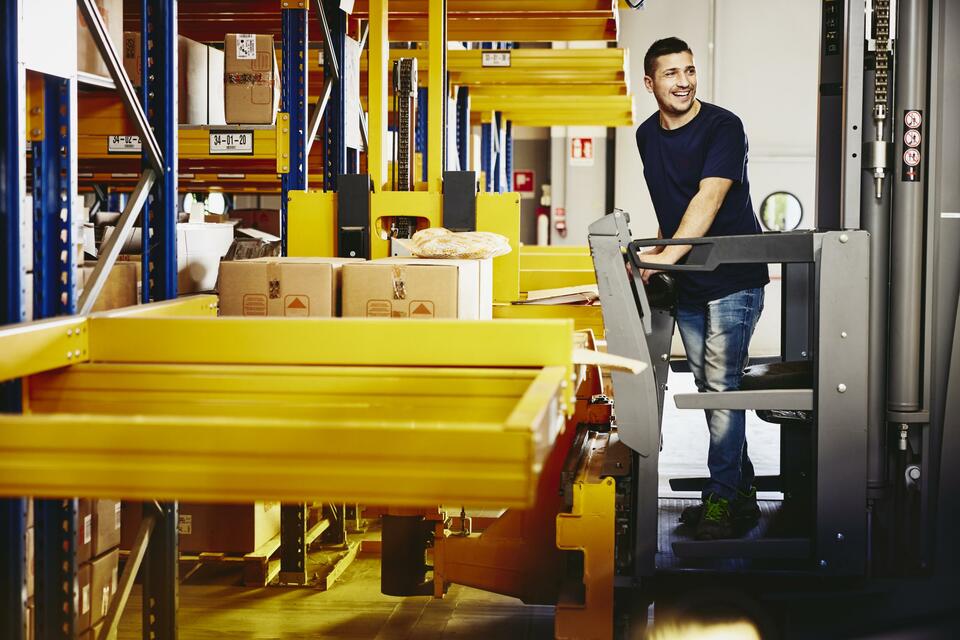 Smiling man standing on a forklift.
