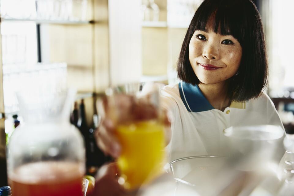 Smiling woman bartender handing a glass of orange juice.